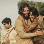 An image of two men hugging in front of others; they're portraying Jesus and Peter in Dallas Jenkins "The Chosen"