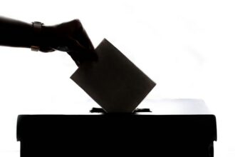 A voter places a ballot into a ballot box behind a privacy screen.