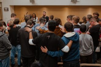Christians gather in fellowship with their arms around one another.