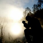 Person kneeling in prayer at sunrise