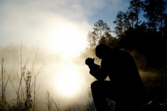 Person kneeling in prayer at sunrise
