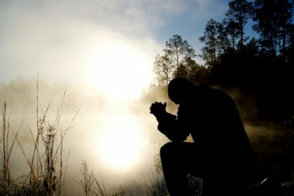 Person kneeling in prayer at sunrise