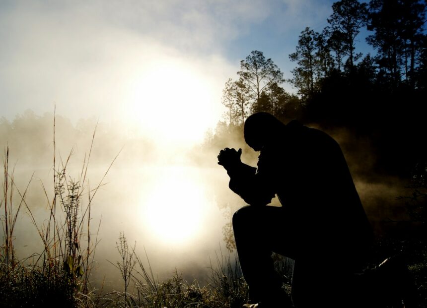 Person kneeling in prayer at sunrise