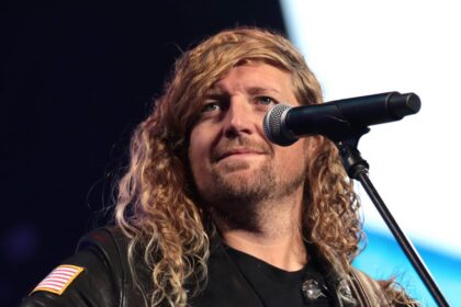 Worship leader Sean Feucht performs with a microphone and guitar at a public event in Phoenix.