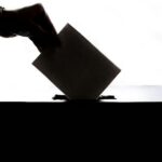 A person placing a ballot into a ballot box. Illustrative photograph.