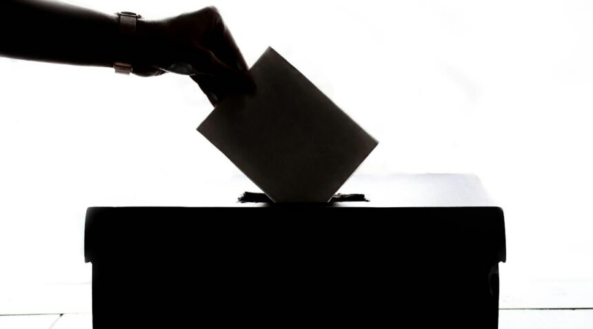 A person placing a ballot into a ballot box. Illustrative photograph.